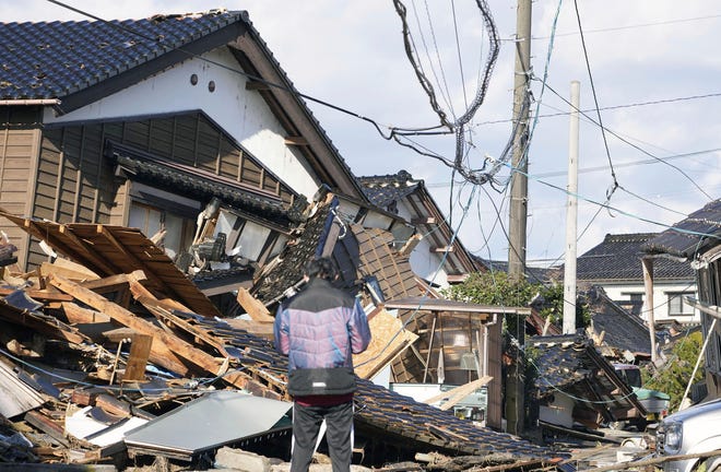 A man stands in front of a fallen house caused by earthquakes in Suzu, Ishikawa prefecture, Japan, Thursday, Jan. 4, 2024. More soldiers have been ordered to bolster the rescue operations Thursday, providing those in need with drinking water hot meals and setting up bathing facilities after a magnitude 7.6 quake hit Ishikawa Prefecture and nearby regions Monday.