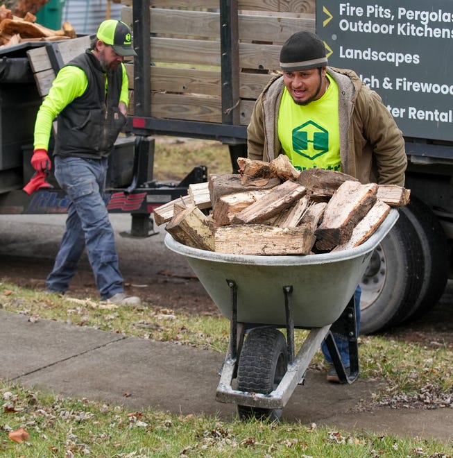 Henry Lopez gives a little extra muscle as he pushes a wheelbarrow over a berm on Thursday, Jan. 4, 2024, as he delivers firewood with Dustin Brown on the northwest side of Indianapolis.
