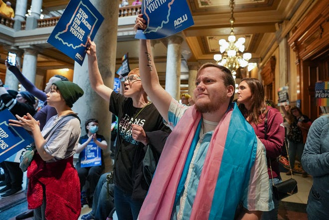 Kristopher Carlock listens to speakers with a transgender pride flag draped around his shoulders Saturday, April 1, 2023, during a Rally to Protect Trans Youth organized by the ACLU of Indiana at the Statehouse in Indianapolis.
